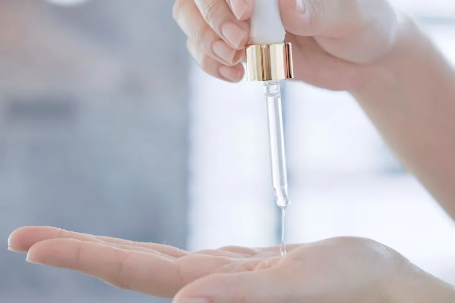 A hand squeezing a dropper of serum onto another hand.